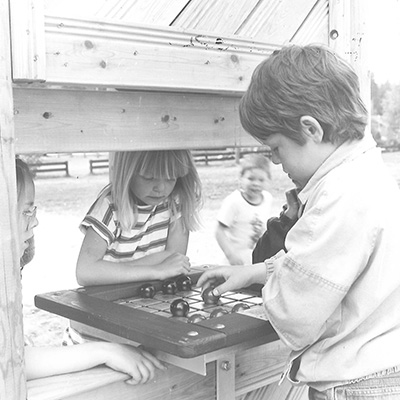 Black and white image of children playing at a playground, it is an old scanned photograph from the 80s.